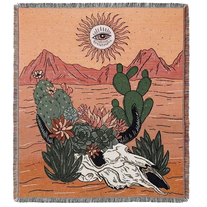 A woven throw blanket featuring a desert landscape with mountains, a sun motif, and various cacti and succulents.