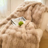 A beige plush faux rabbit fur throw blanket draped over a light-colored sofa with a green apple and a magazine.