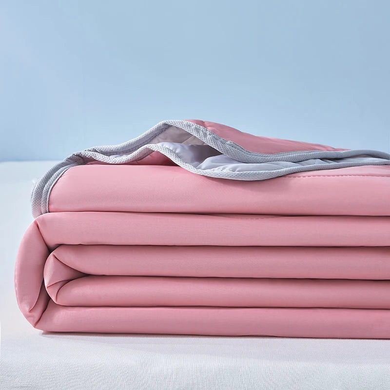 Pink cooling fiber blanket neatly folded on a white surface with a gray fabric band visible.