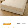 A beige fitted bed sheet is displayed on a modern bed, featuring a textured fabric and a small embroidered design.