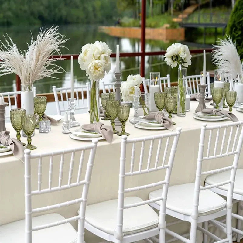 A long white dining table set for an outdoor event with floral arrangements and elegant place settings.