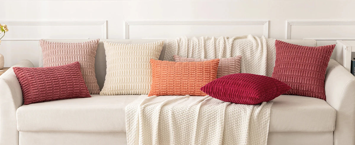 A sofa decorated with various textured throw pillows in shades of pink, beige, and terracotta.