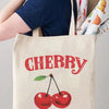 A beige canvas shopping bag featuring the word CHERRY in red script and a small green leaf, with the text HAPPY HAVE A NICE D