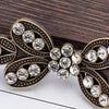 A vintage brass clothing clip featuring intricate scrollwork and clear rhinestones for securing scarves.