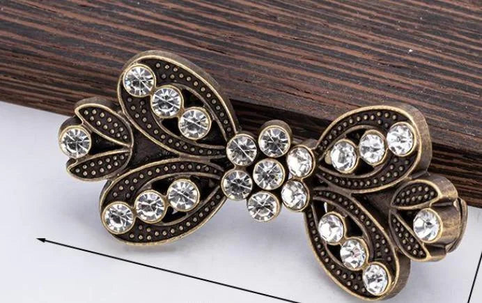 A vintage brass clothing clip featuring intricate scrollwork and clear rhinestones for securing scarves.