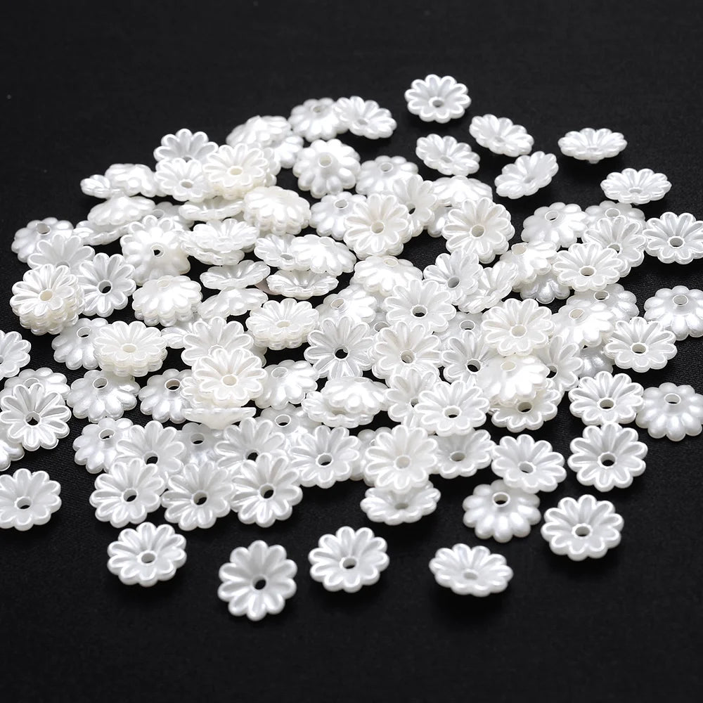 A pile of small, white imitation pearl flower spacer beads for DIY jewelry.