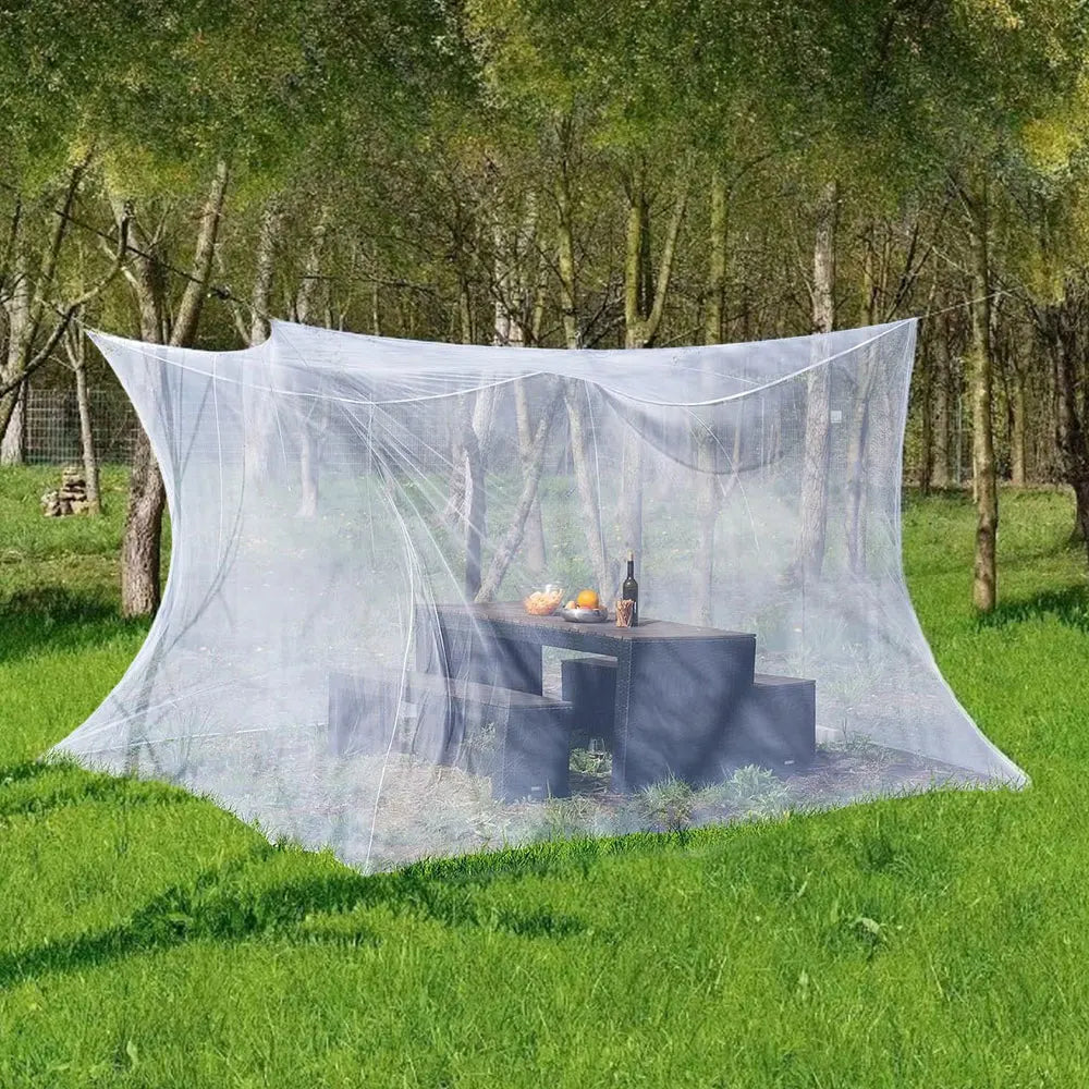 Large outdoor mosquito netting draped over a wooden table in a grassy outdoor setting.