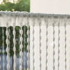 White decorative fabric door curtain with tassel trim hanging in front of a glass surface.