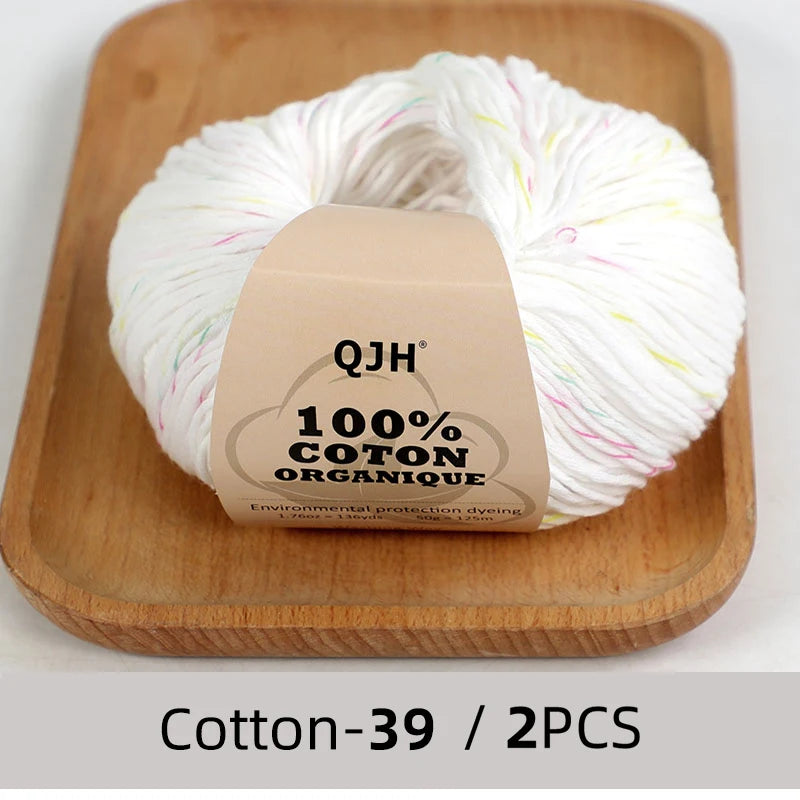 A ball of white organic cotton yarn labeled QJH with the text 100% COTTON ORGANIC shown on a wooden cutting board.