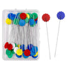 A clear plastic box containing dressmaking pins with colorful, felt-like heads in red, blue, and yellow.