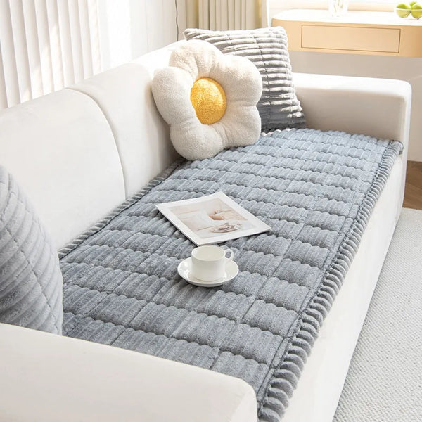 A thick gray flannel sofa pad cover with a yellow pom-pom decoration and a white cup on a white sofa.