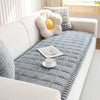 A thick gray flannel sofa pad cover with a yellow pom-pom decoration and a white cup on a white sofa.