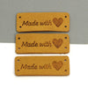 Three rectangular tan leather tags with a heart design are displayed against a gray background.