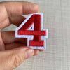A hand holds a red number 4 patch made of white felt for customizable apparel.