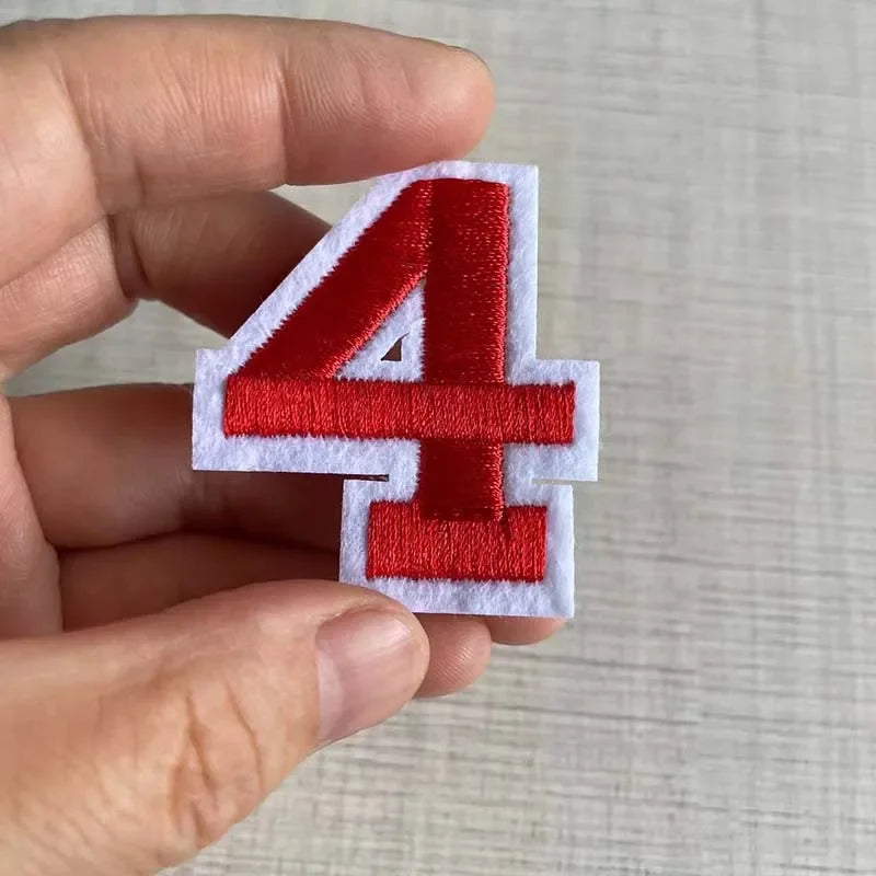 A hand holds a red number 4 patch made of white felt for customizable apparel.