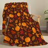 A dark brown fleece throw blanket featuring an orange and red autumn leaf pattern draped over a wooden chair.