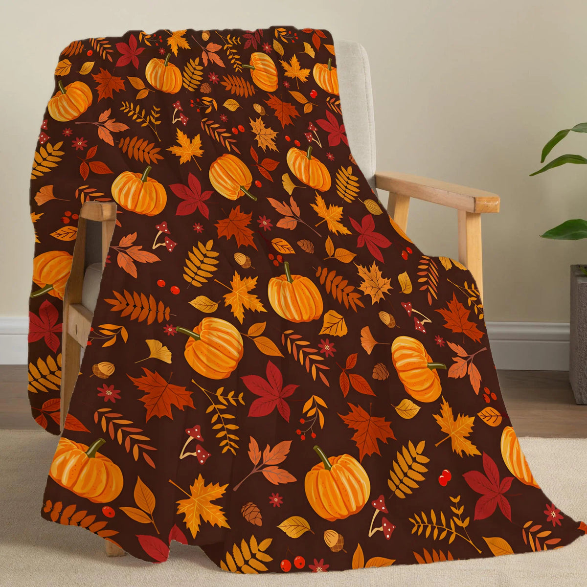 A dark brown fleece throw blanket featuring an orange and red autumn leaf pattern draped over a wooden chair.