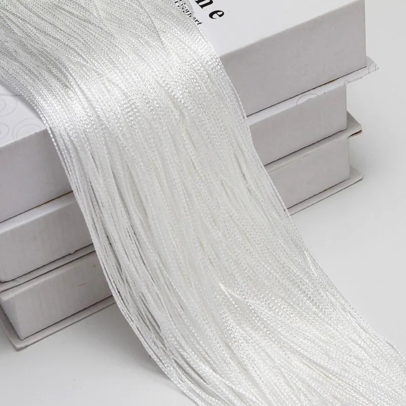 A long, sheer white thread curtain tie-back is draped over a stack of white boxes.