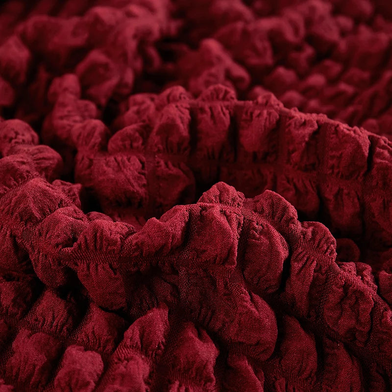 Close-up of a deep red stretch knit sofa cover featuring a textured bubble lattice pattern.