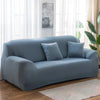 A light blue stretch sofa cover with gray throw pillows placed in a bright living room.