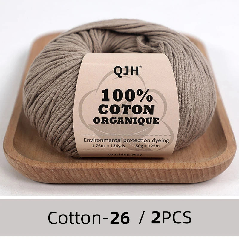 A ball of natural gray organic cotton yarn labeled QJH 100% COTON ORGANIQUE resting on a wooden tray.