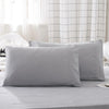 A stack of solid gray microfiber pillow covers on a bed with white curtains.