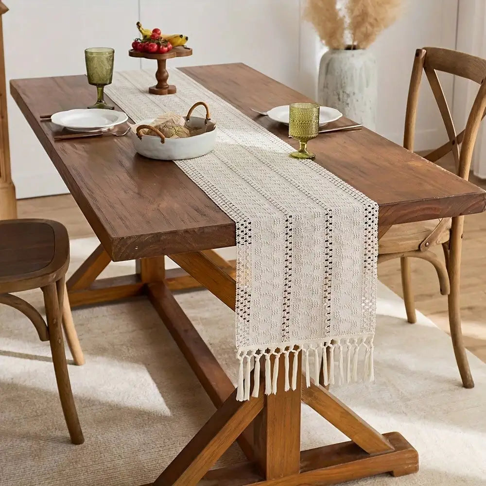 A wooden dining table set with a beige tasseled table runner and rustic decor.
