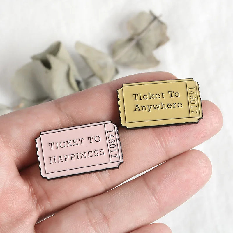 Two vintage enamel airline ticket lapel pins, one gold and one pink, are held in a hand against a white background.