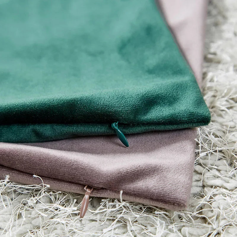 A dark green velvet throw pillow cover is folded next to a dusty rose colored one on a fluffy white surface.