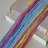 Colorful decorative door string curtains in various shades of red, blue, green, and purple stacked on white books.