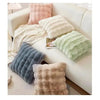 A collection of fluffy winter throw pillows in shades of beige, pink, and green arranged on a white sofa.