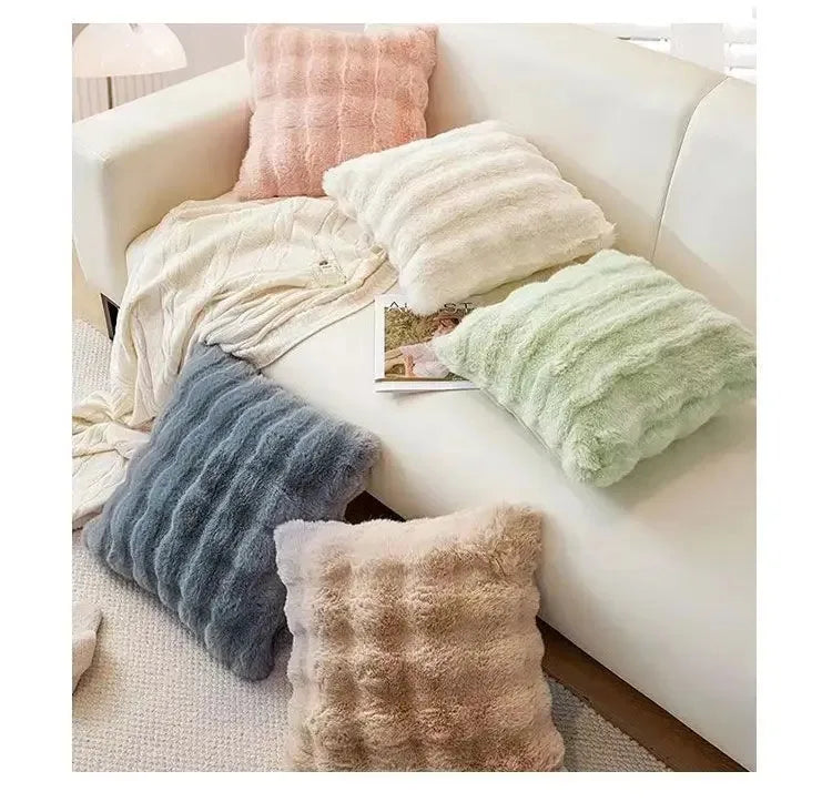 A collection of fluffy winter throw pillows in shades of beige, pink, and green arranged on a white sofa.