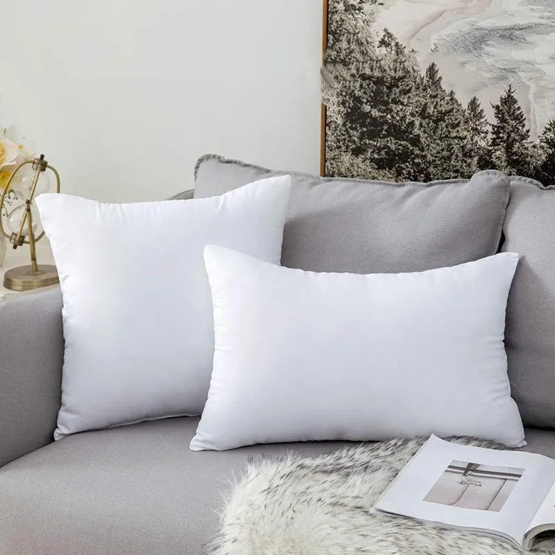 A white throw pillow insert with bounce-back support resting on a gray sofa.