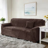 A dark brown stretch velvet sofa slipcover resting on a light gray fluffy rug in a bright room.