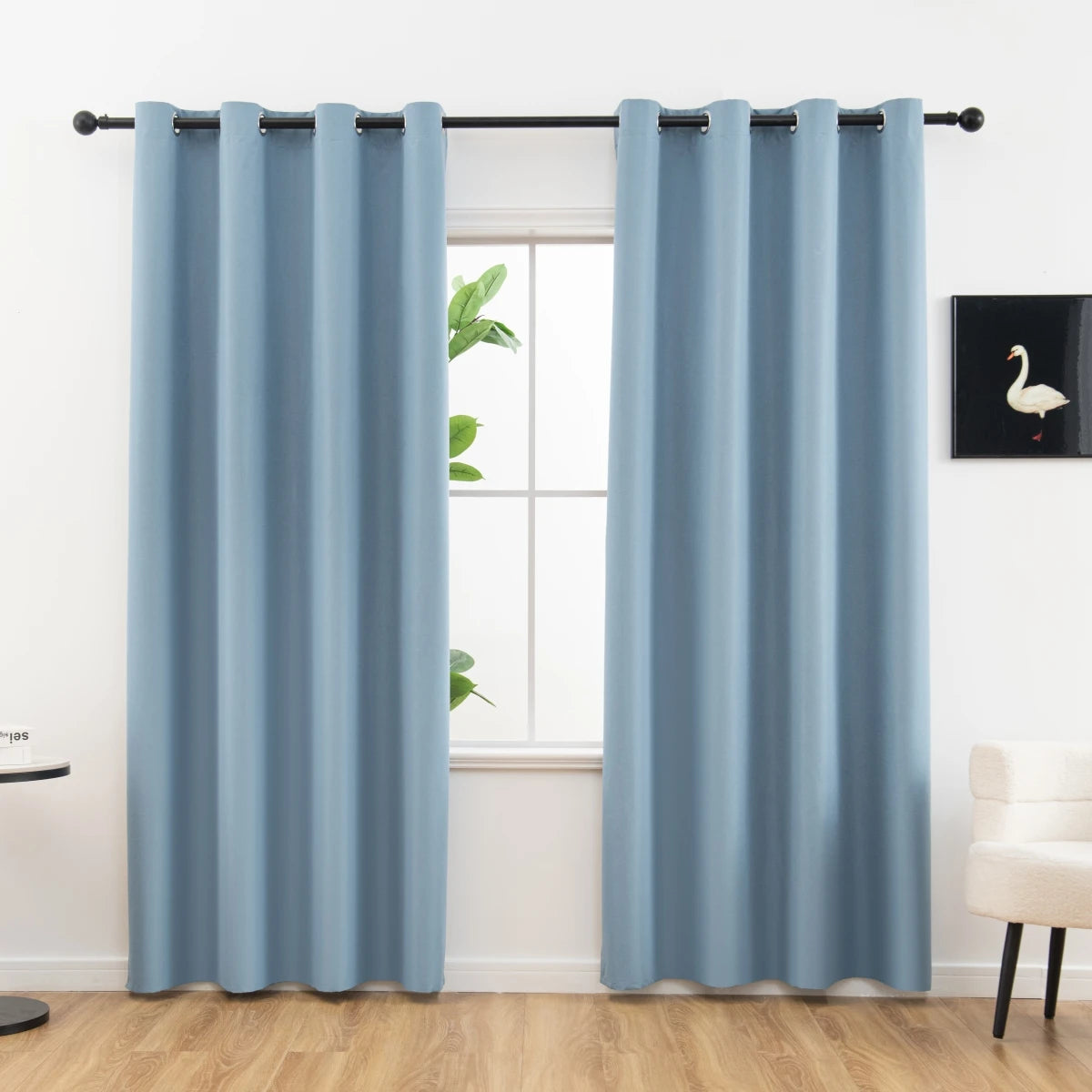 A set of two modern light blue blackout grommet curtains hanging in a window frame.