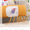 A ball of yellow-orange hand-woven cotton yarn is displayed next to a ruler, showing the thread for crafting.