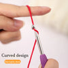 A hand is holding a red thread attached to a silver precision aluminum crochet hook with a purple grip, demonstrating a curve