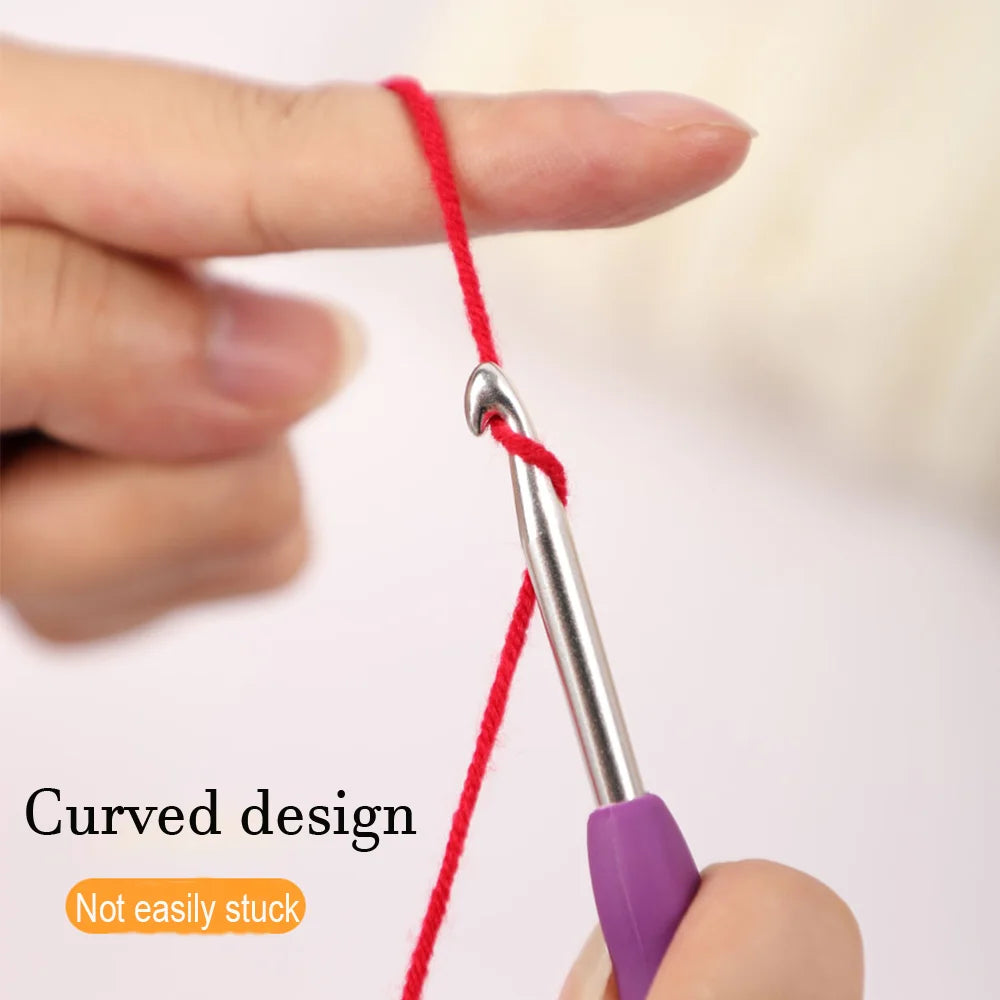 A hand is holding a red thread attached to a silver precision aluminum crochet hook with a purple grip, demonstrating a curve