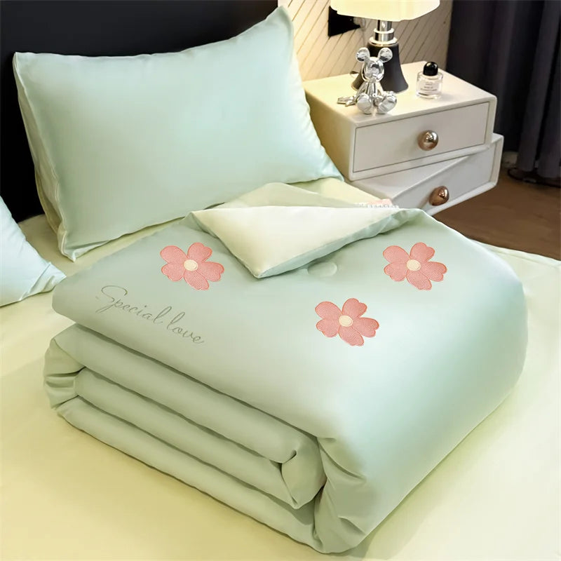 Light mint green embroidered cooling summer quilt folded on a bed with a bedside table.