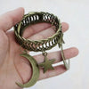 A hand holds a vintage gold-toned metal curtain clip featuring an intertwined wreath design with a crescent moon and a star c