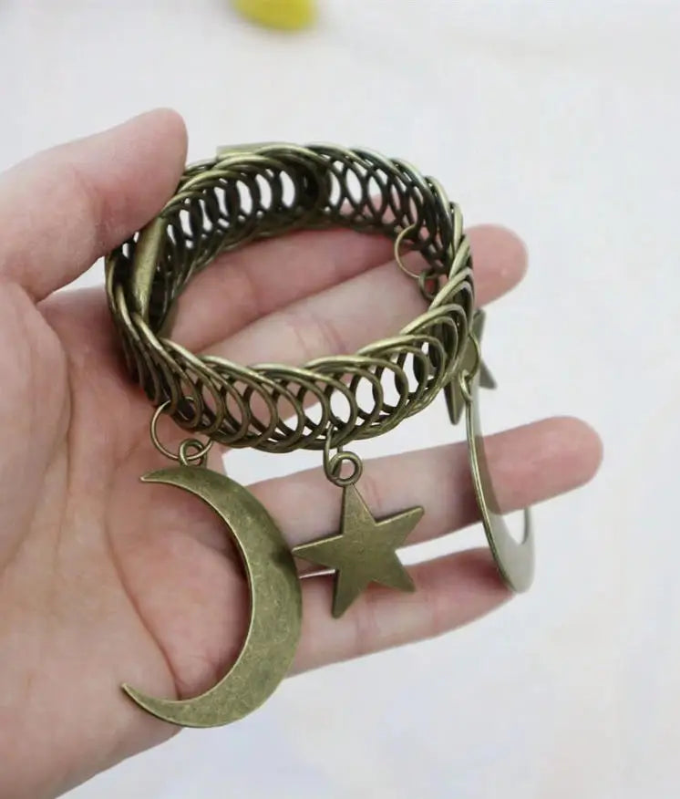 A hand holds a vintage gold-toned metal curtain clip featuring an intertwined wreath design with a crescent moon and a star c