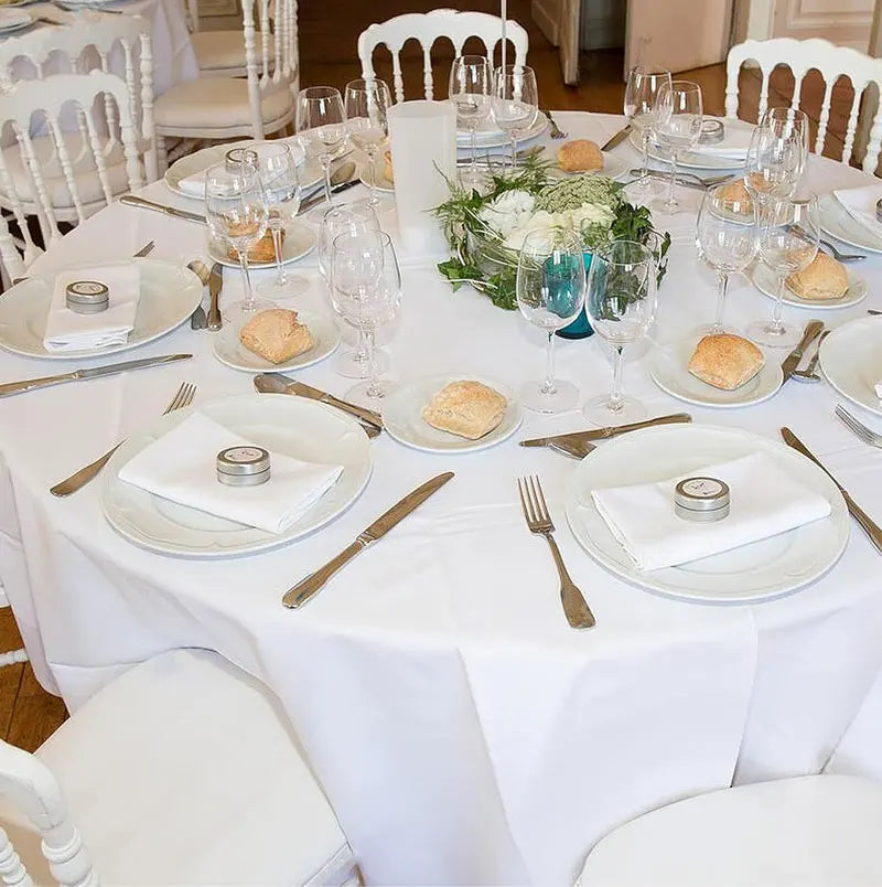 Elegant white satin round tablecloths set for a formal dining event with silverware and glassware