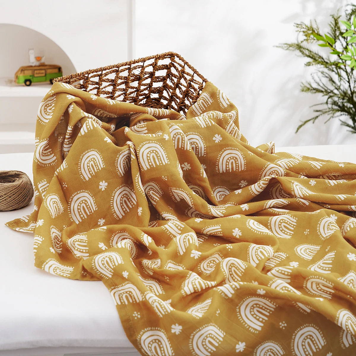 A yellow muslin swaddle blanket with white rainbow patterns is draped on a white surface.