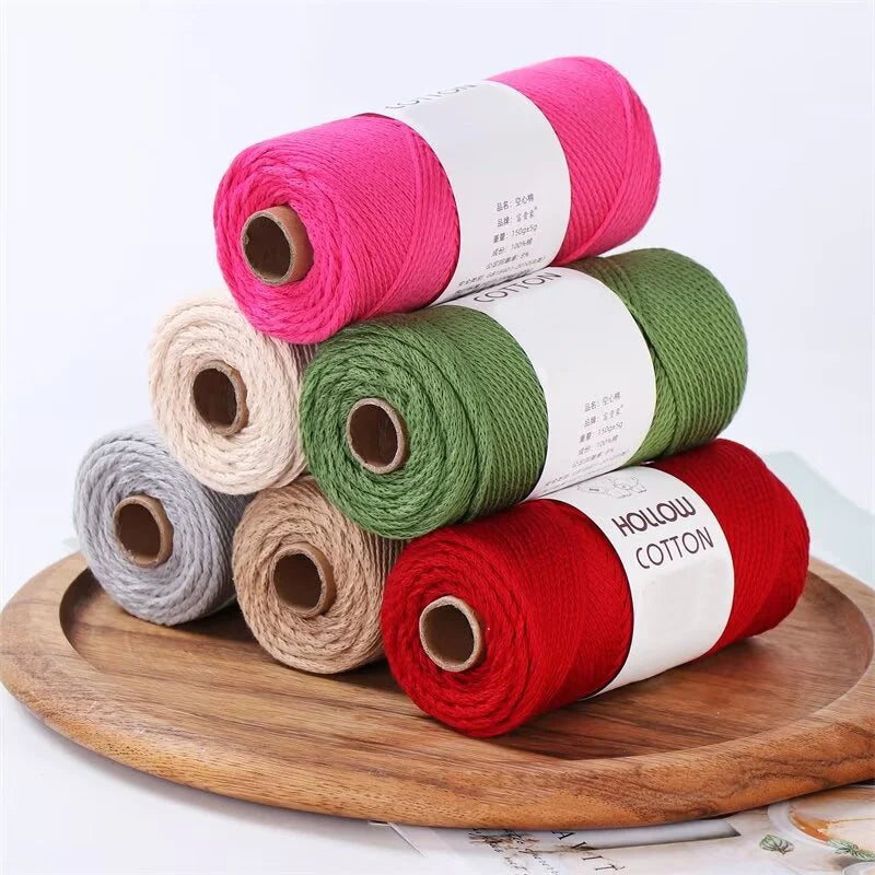 A stack of hand-knitted cotton yarn in various shades of pink, green, and red on a wooden board.