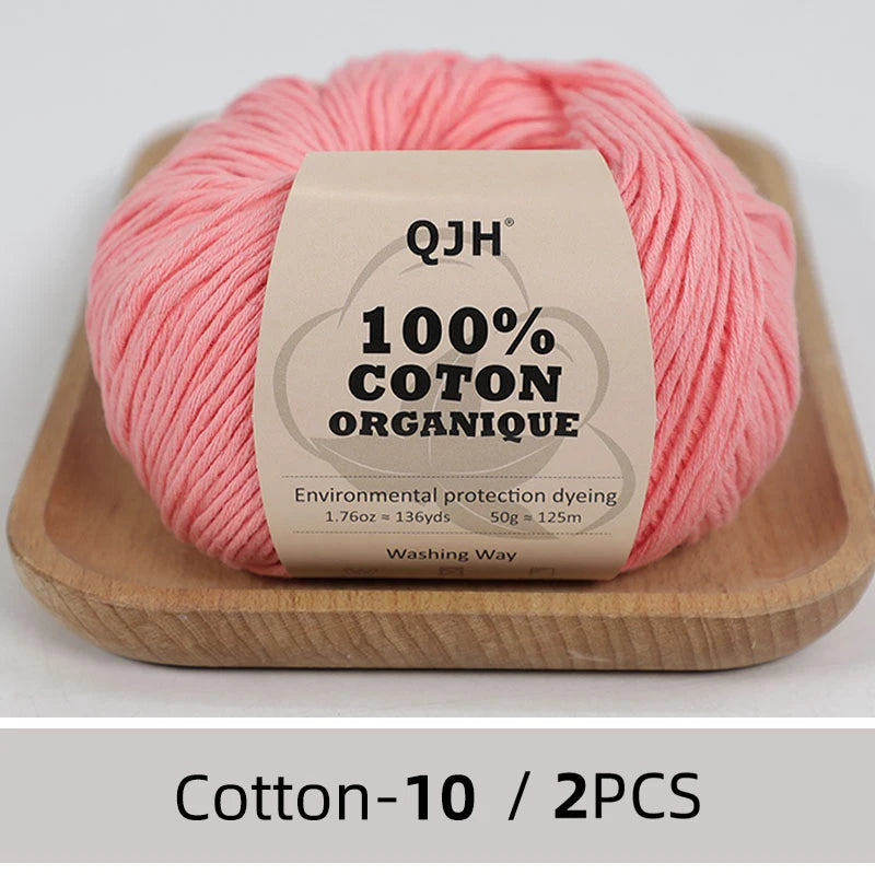 A ball of pink organic cotton yarn labeled QJH 100% COTON ORGANIQUE resting on a wooden tray.