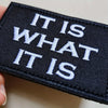 Black embroidered patch with white text reading IT IS WHAT IT IS
