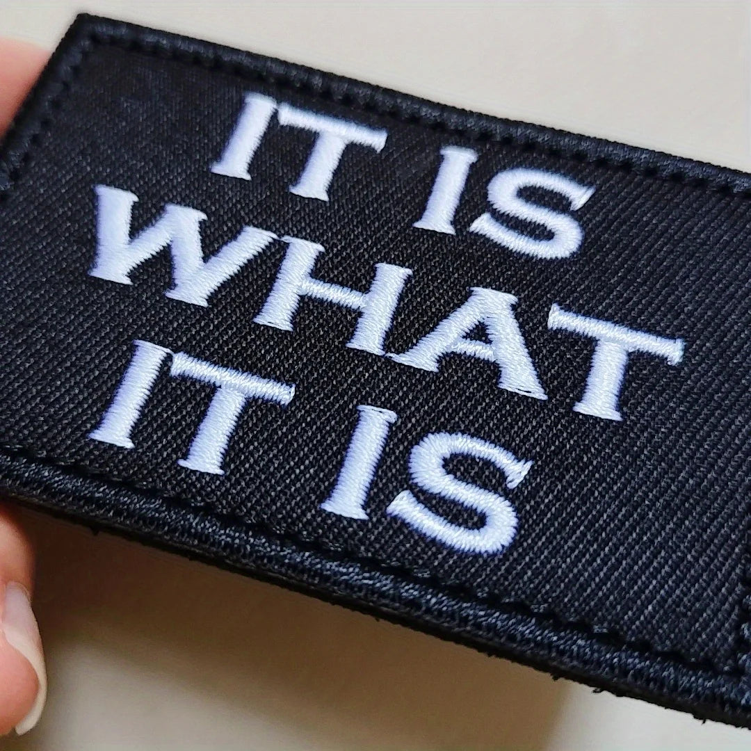 Black embroidered patch with white text reading IT IS WHAT IT IS