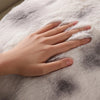A hand rests on a soft, gray and white faux rabbit fur textile.