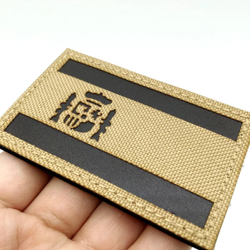 A rectangular tactical patch featuring the Spanish flag design with a hook and loop backing on a beige fabric.