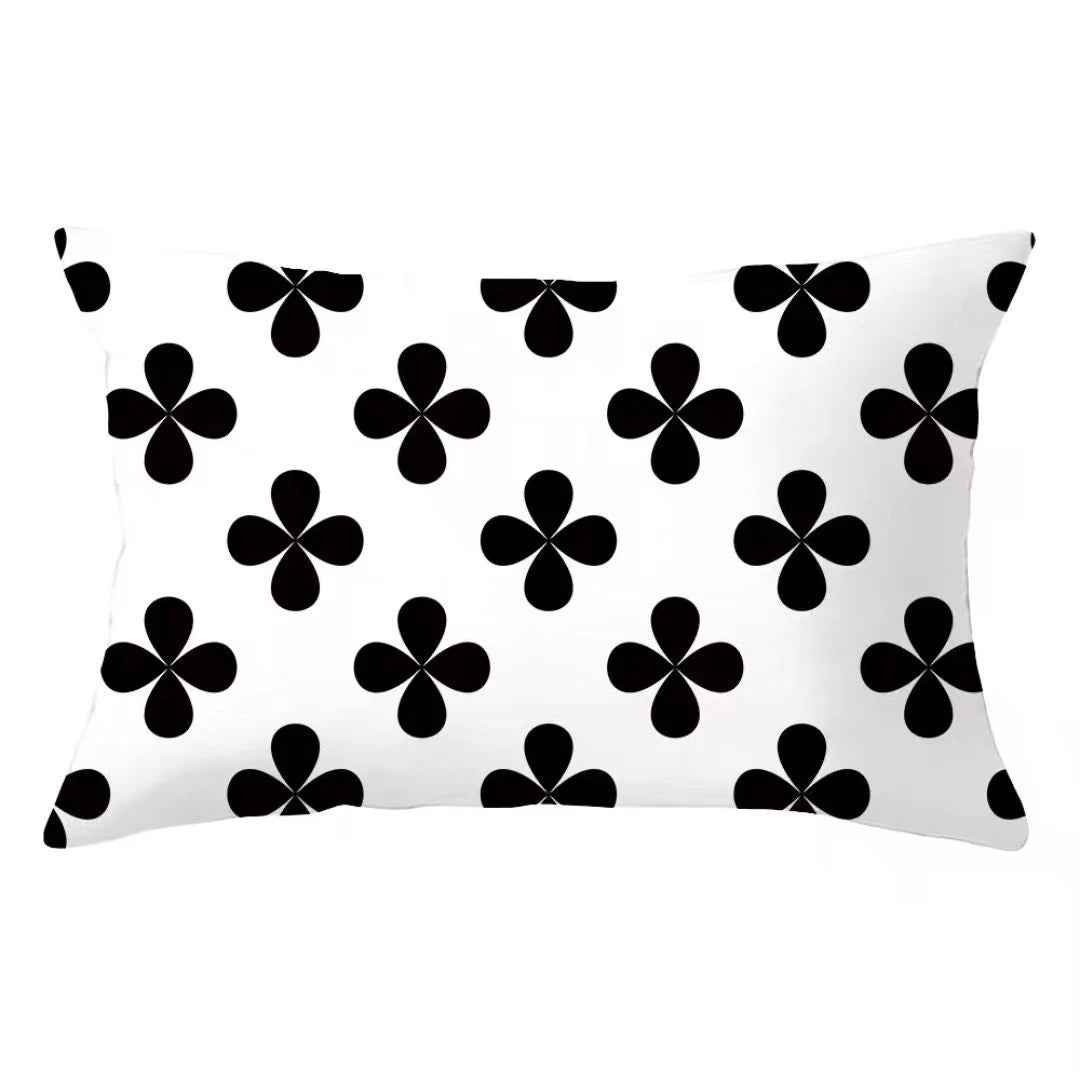A white decorative pillow cover featuring a repeating pattern of black four-leaf clovers.